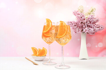 Festive alcoholic cocktail Aperol spritz in glasses on a bright background with a bouquet of lilacs, summer bar concept, alcoholic drinks at a party, restaurant and cafe advertising, selective focus.