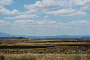 Obraz premium A panoramic view of the vast, open landscape in Las Bardenas Reales, Spain, featuring rolling hills and a clear, blue sky with scattered clouds.