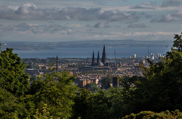 View of Edinburgh’s skyline and Saint Mary’s Cathedral, with green trees in the foreground, and...