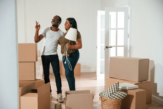 Woman is holding lamp. African American couple are moving into new house - Powered by Adobe