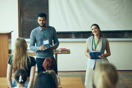 Two teachers, man and woman standing in university classroom and leading meeting with students. Talking about upcoming exams. Concept of education, youth, workshop, knowledge