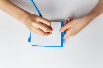 hand holding blue pencil and writing in notebook on white background isolated copy space