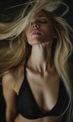 Fototapeta premium A young blonde woman in a black top with closed eyes and flowing hair, exuding confidence and beauty in a dramatic, moody setting