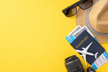 Top view of travel essentials such as passport, boarding pass, camera, sunglasses, and hat on a vibrant yellow background