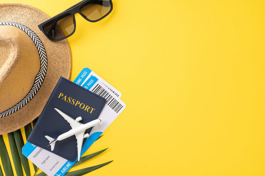 Flat lay of travel essentials including a straw hat, sunglasses, passport, and flight tickets on a vibrant yellow background