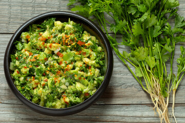 Guacamole with a lot of chopped fresh coriander, topped with hot chili flakes. A bunch of freshly harvested coriander with roots on the side.