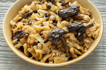 Sauerkraut with dried wild mushroom and laurel leaves, decorated with three halved mushrooms. Rustic wooden table.
