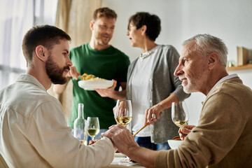 A gay couple sits at a table with parents, enjoying a meal and conversation.