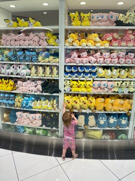 Tokyo, Japan - May 2nd, 2024: A little girl reaching for a stuffed pokemon toy amongst hundreds on the shelves, at the Pokemon Center Mega Tokyo, in Tokyo, Japan.