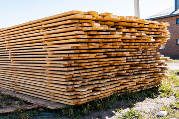 In an outdoor industrial yard, a large stack of neatly arranged cut lumber boards is ready for construction projects, showcasing sustainable use of natural material