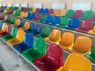 Multicolored Empty plastic chairs in the stands of the stadium. Many empty seats for spectators in...