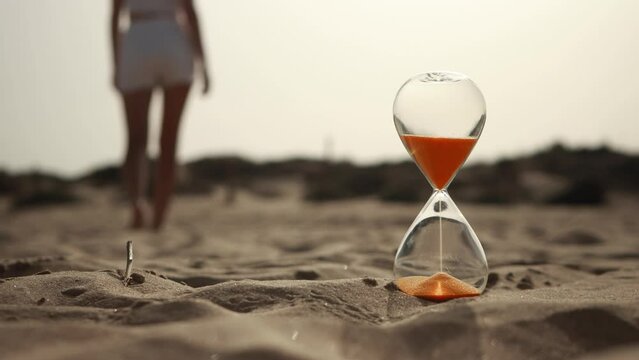 In foreground there is an hourglass in background,girl walk along beach at sea, summer beach holiday, time travel. Clock glass Tropical summer beach, sea wave on sunny day. Hourglass shore of blue sea