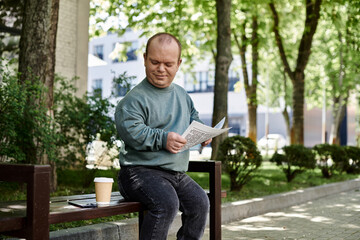 Obraz premium A man with inclusivity sits on a park bench, reading a document and enjoying a cup of coffee.