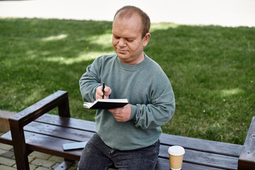 A man with inclusivity sits on a park bench writing in a notebook, enjoying a peaceful moment...