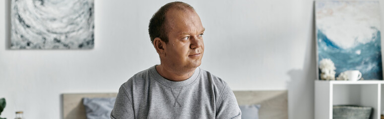 Obraz premium A man with inclusivity sits on a bed, contemplating the day ahead in a bright and airy room.