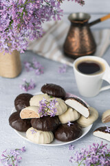 Cup of coffee, lilac, marshmallow in dark and white chocolate glaze on plate, cezve. Still life