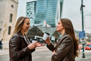 Two businesswomen enjoying a coffee break outside their office.