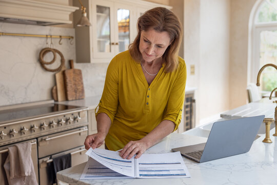 Senior woman looking at paperwork and using a laptop computer for financial investment