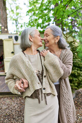 Fototapeta premium A middle-aged lesbian couple shares a tender moment while camping in a lush green forest, enjoying the beauty of nature together.