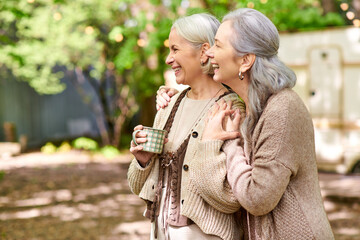 Fototapeta premium Two middle-aged women laugh together while enjoying a cup of coffee during a camping trip.