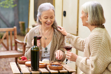 Two women enjoy wine and laughter while camping in the forest.