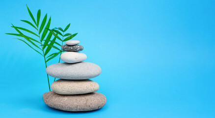 Pyramid of pebbles on a blue background next to palm leaves. Summer background