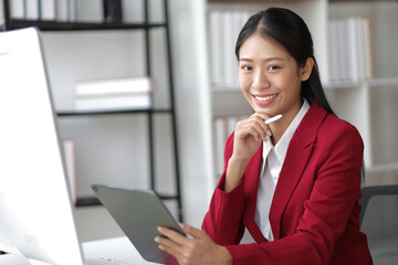 Portrait of attractive Asian businesswoman sitting at desk in office.