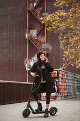 Young woman talking on her smartphone while standing with an electric scooter on an autumn day in a city street..