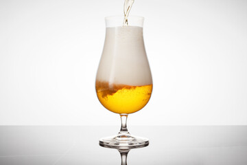 Glass of pouring light beer on a white background and marble table.