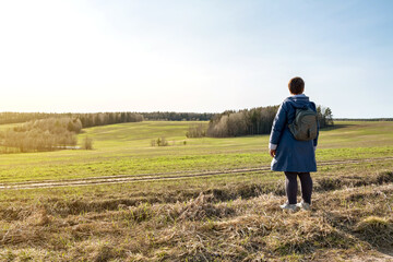 An elderly woman walks along a spring field alone.