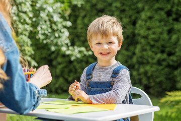 Smiling child coloring with mother outside. Early years. Baby development.