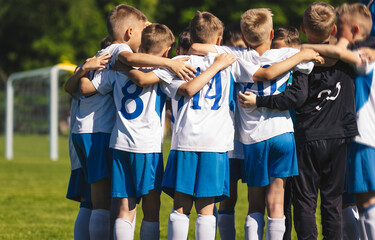 Obraz premium Happy Boys Huddling United in Sports Team. Kids Building Team Spirit Altogether With a Coach. Boys in Sporty Uniforms Play Sports Game Outdoor