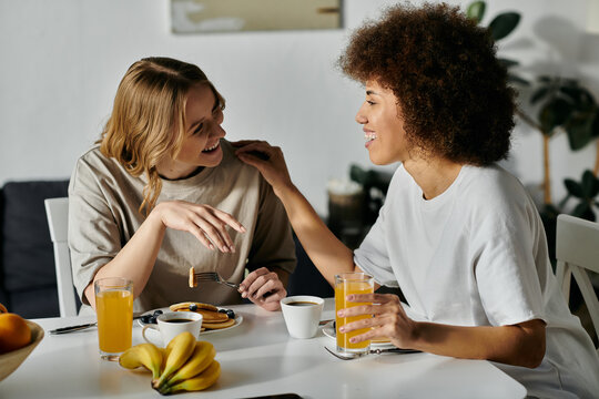 Two women, dressed casually, share a meal and laughter at home.