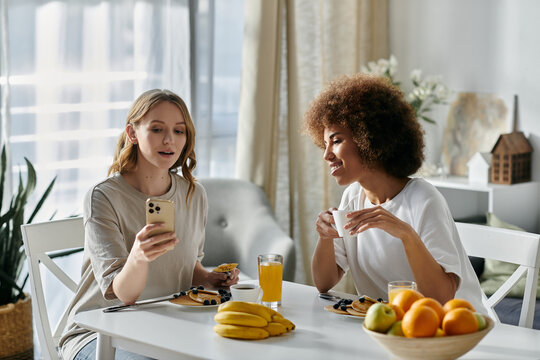 Two women enjoy a leisurely morning together at home, sharing a meal and laughter.