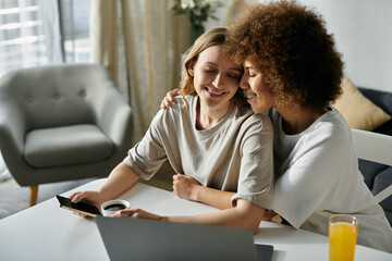Two women, a lesbian couple, cuddle while using a laptop and enjoying a beverage.