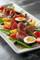 Gourmet seared tuna salad with colorful vegetables, boiled eggs, and fresh greens on a white rectangular plate.