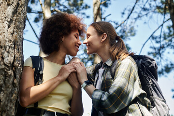 A young lesbian couple enjoys a romantic moment while hiking through a lush forest.