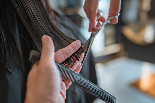 Closeup - Hands of Hairdresser trimming black hair with scissors at hair salon - Powered by Adobe