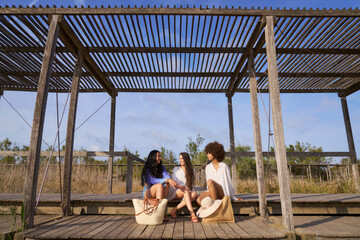 Three women sitting on a wooden platform, one of them holding a purse