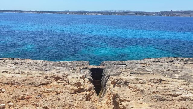 Cut in the rocks leading towards the sea, Comino island and Malta in the background. High quality 4k footage