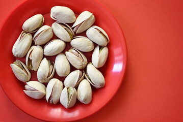 Pistachios in a red dish on red background top view