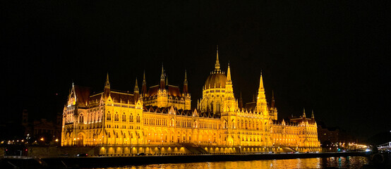 Fototapeta premium Night time Cruising past the Budapest Parliament Building illuminated at night. A beautiful building lit by golden lights, situated on the edge of the River Danube.