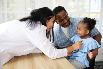 Obraz premium asian doctor holding stethoscope and listening to African child patient's breath beside her father in the clinic