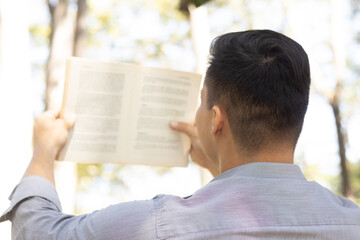 Naklejka premium young latin man reading a book in nature with his back turned