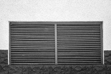Big ventilation grille on gray wall. Grille is made of metal, with grid-like pattern that allows air to pass through while preventing debris from entering. Black and white photo. Close-up. Copy space