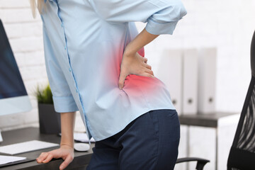Woman suffering from pain in lower back at workplace in office, closeup