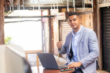 young latin freelance man with cell phone and laptop working in a beautiful town with elegant suit