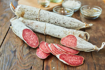 The cured sausage, cut into slices, lies on a wooden surface surrounded by spices. Meat production.