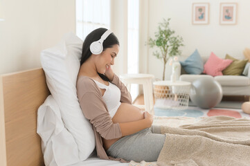 Happy pregnant woman with headphones listening to mozart music and lying on bed, pregnancy concept