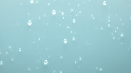 A close-up image of numerous water droplets scattered on a smooth, light blue surface.
